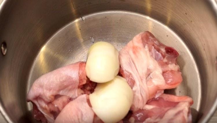Nous répandons la viande de poulet dans la casserole, ajoutons l'oignon coupé en deux.