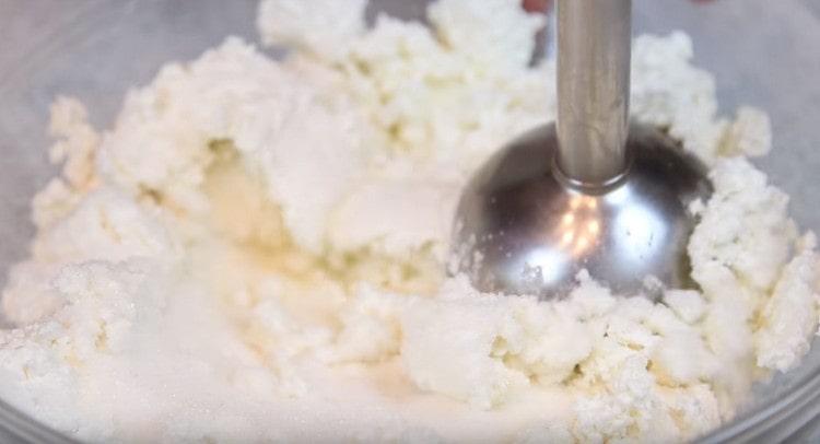 Nous interrompons le fromage cottage avec du sucre avec un mélangeur à main.