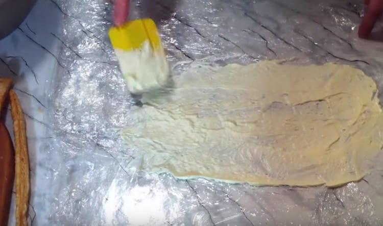 We cover the working surface with cling film and grease it with cream.
