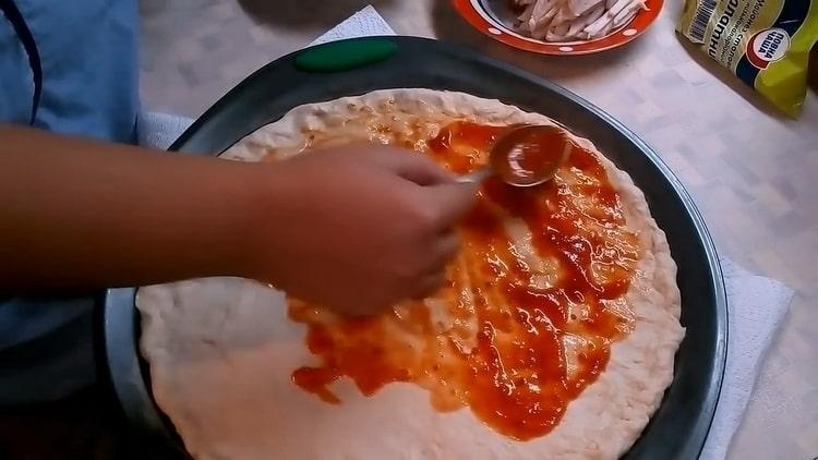 Upang makagawa ng pizza na may mga kabute at keso, grasa ang kuwarta na may sarsa