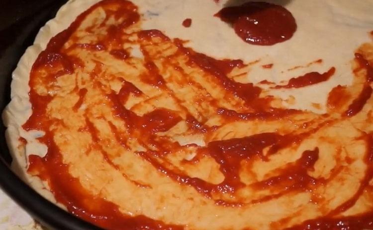 Para hacer pizza con salchichas y queso, ponga la salsa sobre la masa