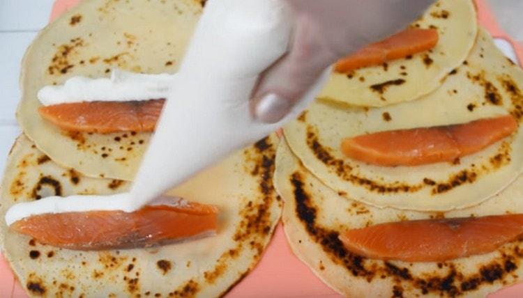 Extendemos un trozo de salmón en cada panqueque y exprimimos el queso crema cerca de él.