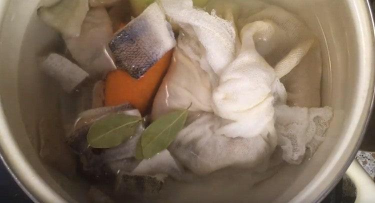 Llenamos el nudo con los restos de pescado, las rodajas en sí, así como cebollas, guisantes, guisantes, zanahorias y hojas de laurel con agua en una cacerola.
