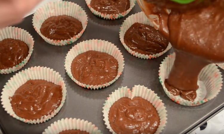 Having put paper inserts in the cupcake molds, fill them with dough.