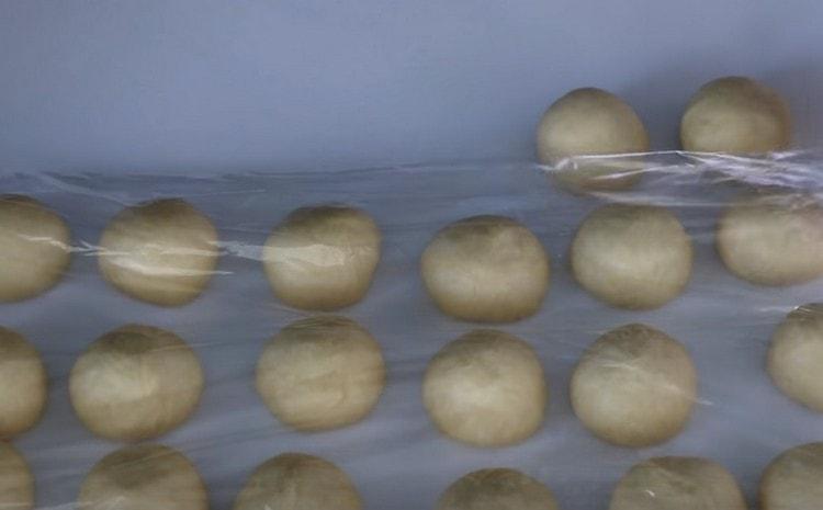 Having rolled balls from dough pieces, we cover them with cling film.