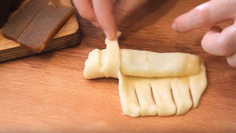 Faire des coupes sur le bord libre de la pâte, envelopper les bandes résultantes sur un morceau de pâte dans une confiture.