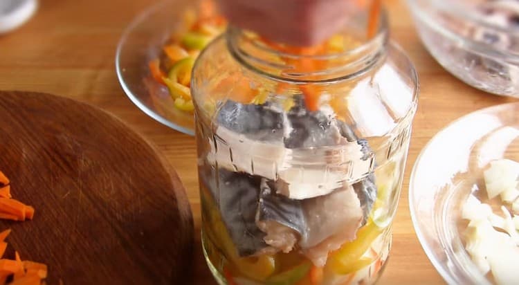 At the bottom of the jar we put a bay leaf, and on top of it we make layers of onions, carrots, peppers and mackerel.