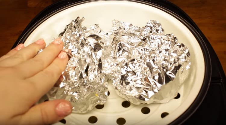 Sur le dessus des pommes de terre, nous plaçons le panier du multicuiseur pour la cuisson à la vapeur et y mettons le poisson emballé dans du papier d'aluminium.