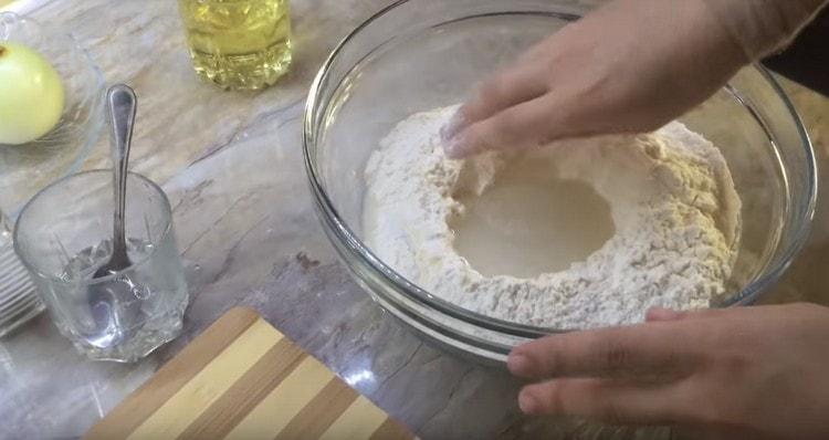 Versez de l'eau dans le sillon de la farine, mais pas en une fois.