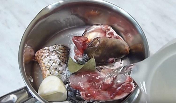We put the head and tail of the carp in the pan, add the onion, bay leaf and fill it with water.