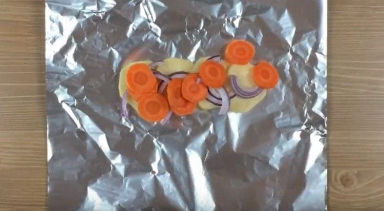 mettre les pommes de terre sur un morceau de papier d'aluminium, ajouter les oignons et les carottes dessus.