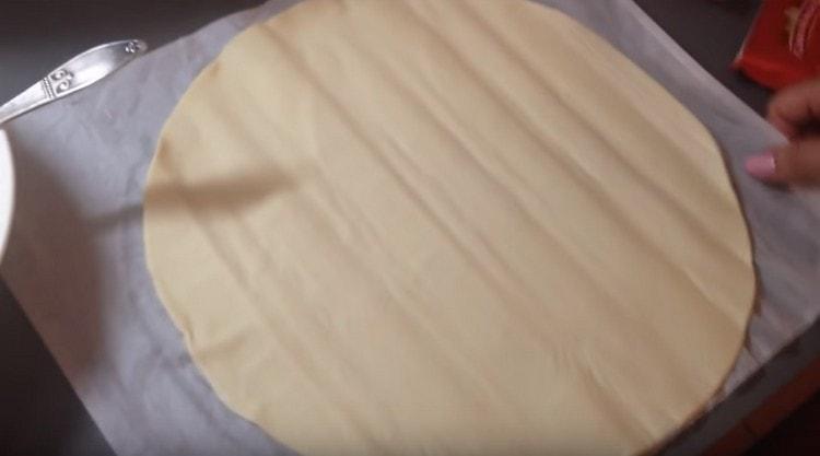 Sur la plaque à pâtisserie, nous étalons le parchemin et y posons la pâte feuilletée roulée.