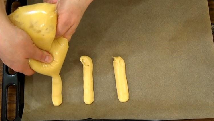 Nous plantons de longs flans pour les éclairs sur une plaque à pâtisserie recouverte de parchemin.