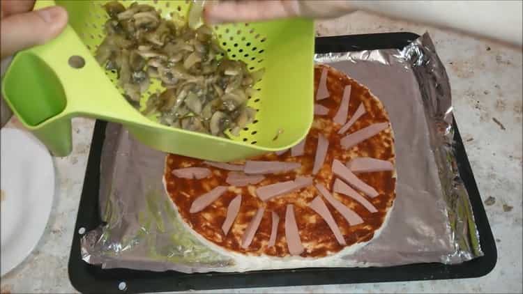 Para preparar pizza con salchichas y queso, ponga el relleno sobre la masa.