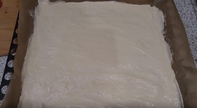 Pizza dough made on kefir is evenly distributed on a baking sheet covered with parchment.