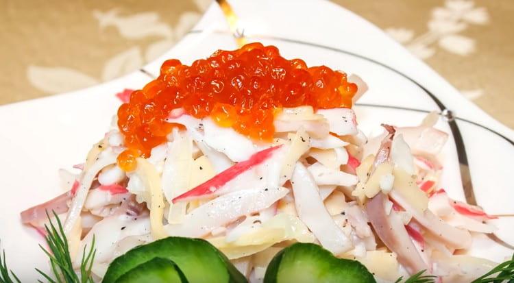 Al servir, la ensalada con palitos de calamares y cangrejo está decorada con caviar rojo.