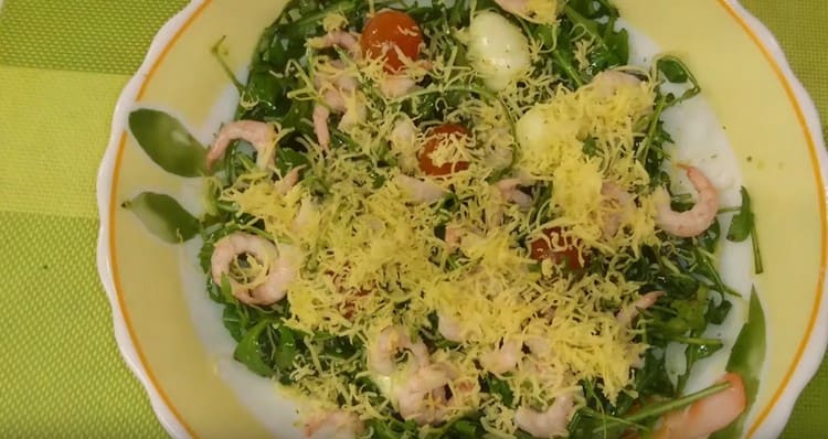 Salade prête à la roquette, aux crevettes et aux tomates cerises saupoudrer de fromage râpé.