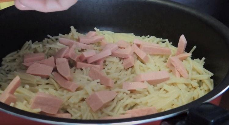 Sur les pâtes, étalez des morceaux de saucisse.