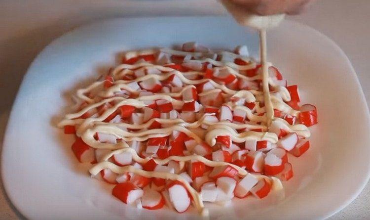 Coloque una capa de palitos de cangrejo en un plato, engrase con mayonesa.