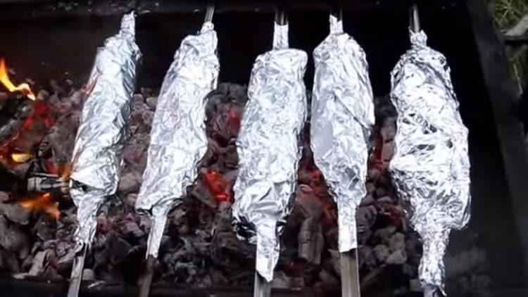 Shish kebabs wrapped in foil are returned to the barbecue.