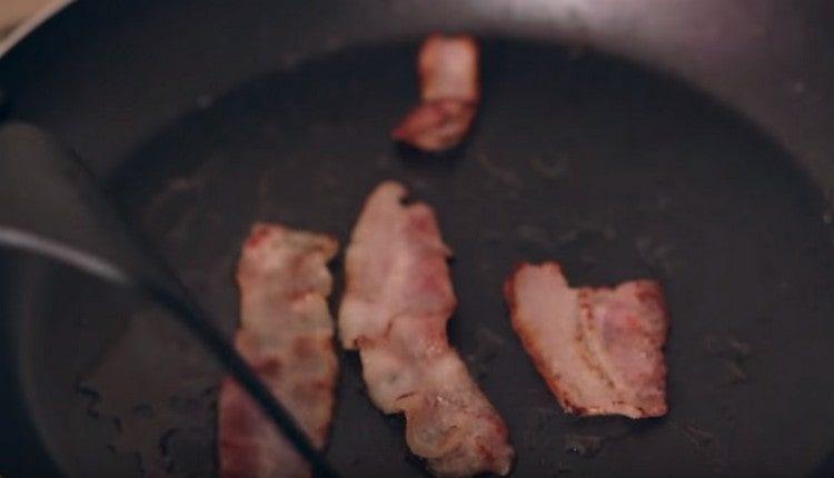 Fry thin slices of bacon in a pan.