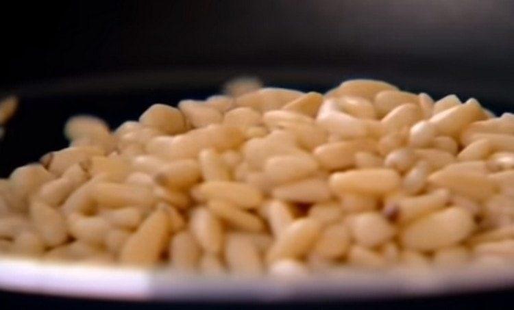 In a dry frying pan, fry pine nuts.