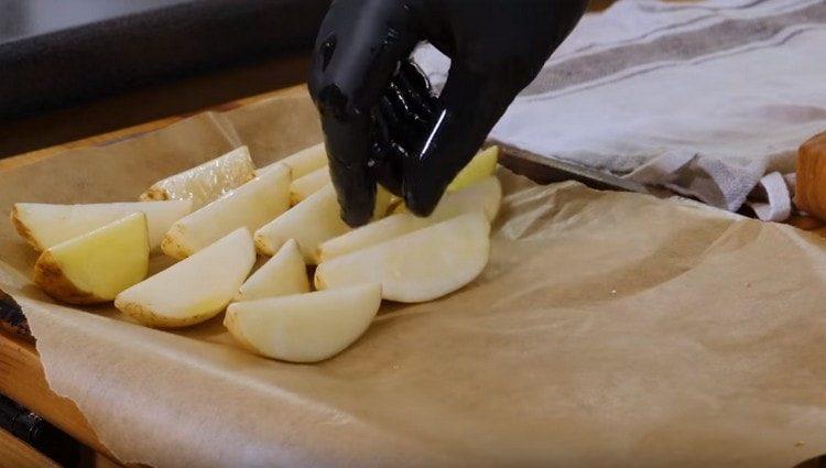 posant une plaque à pâtisserie avec du parchemin, mettez dessus des quartiers de pomme de terre.