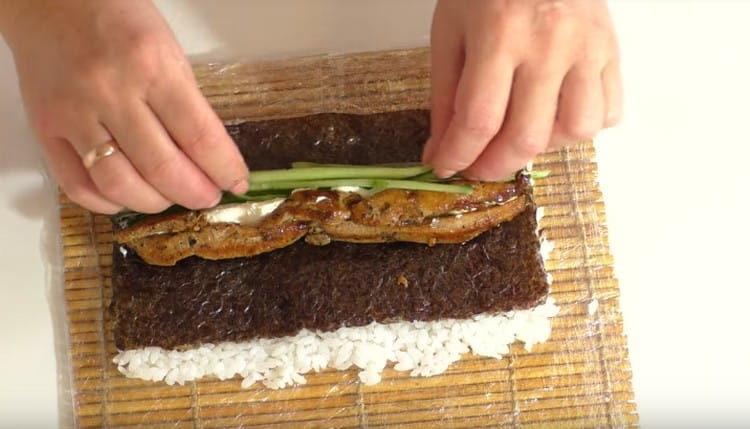 We turn the nori leaf with rice down and put chicken, cucumbers, green onion feathers, and cream cheese on it.