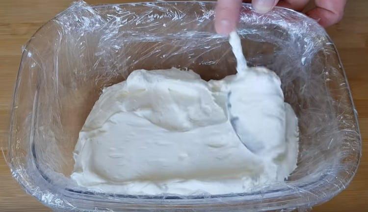 Nous recouvrons le moule à gâteau d'un film plastique et graissons le fond avec de la crème.